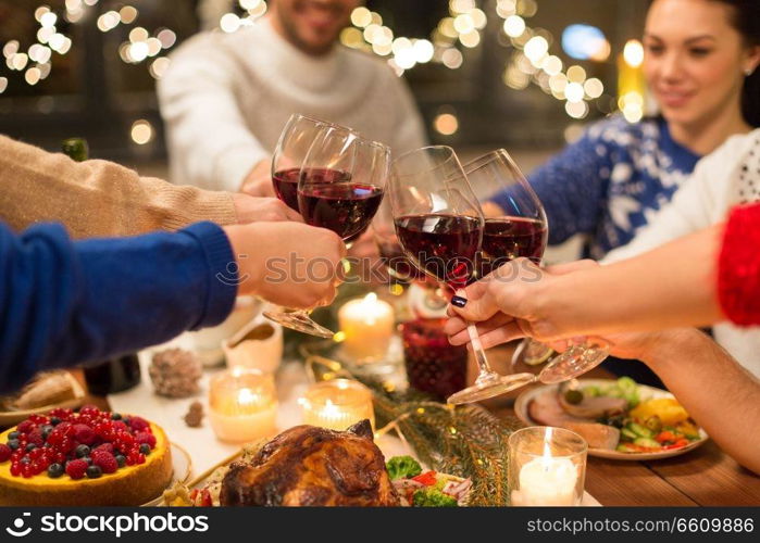 holidays and celebration concept - close up of happy friends having christmas dinner at home, drinking red wine and clinking glasses. close up of friends with wine celebrate christmas