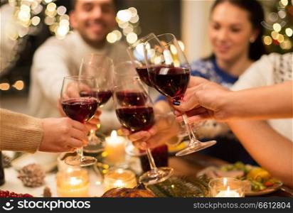holidays and celebration concept - close up of happy friends having christmas dinner at home, drinking red wine and clinking glasses. close up of friends with wine celebrate christmas