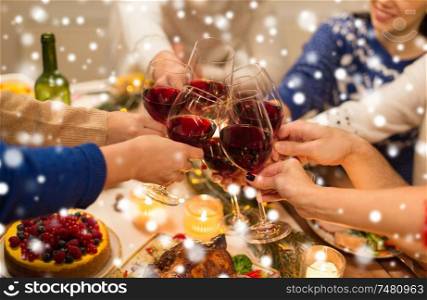 holidays and celebration concept - close up of happy friends having christmas dinner at home, drinking red wine and clinking glasses over snow. close up of friends with wine celebrate christmas