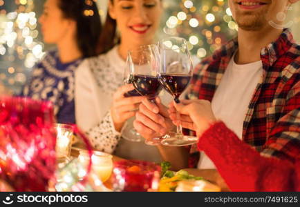 holidays and celebration concept - close up of happy friends having christmas dinner at home, drinking red wine and clinking glasses. close up of friends with wine celebrate christmas