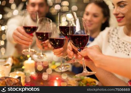 holidays and celebration concept - close up of happy friends having christmas dinner at home, drinking red wine and clinking glasses. close up of friends with wine celebrate christmas
