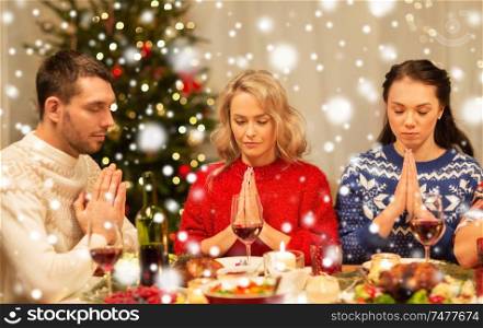 holidays and celebration concept - friends holding hands and praying before christmas dinner at home over snow. friends praying before christmas dinner at home