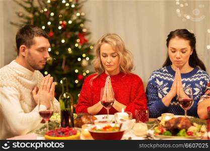 holidays and celebration concept - friends holding hands and praying before christmas dinner at home. friends praying before christmas dinner at home