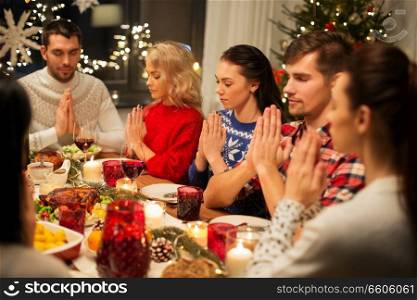 holidays and celebration concept - friends holding hands and praying while having christmas dinner at home. friends having home christmas dinner and praying