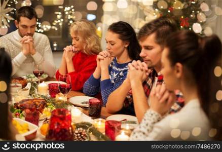 holidays and celebration concept - friends holding hands and praying while having christmas dinner at home. friends having home christmas dinner and praying