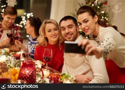 holidays and celebration concept - happy friends having christmas dinner at home and taking selfie by smartphone. friends having christmas dinner and taking selfie