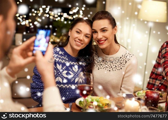 holidays and celebration concept - happy friends having christmas dinner at home and taking picture by smartphone over snow. friends having christmas dinner and taking picture