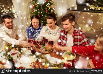 holidays and celebration concept - happy friends having christmas dinner at home, drinking red wine and clinking glasses over snow. friends celebrating christmas and drinking wine