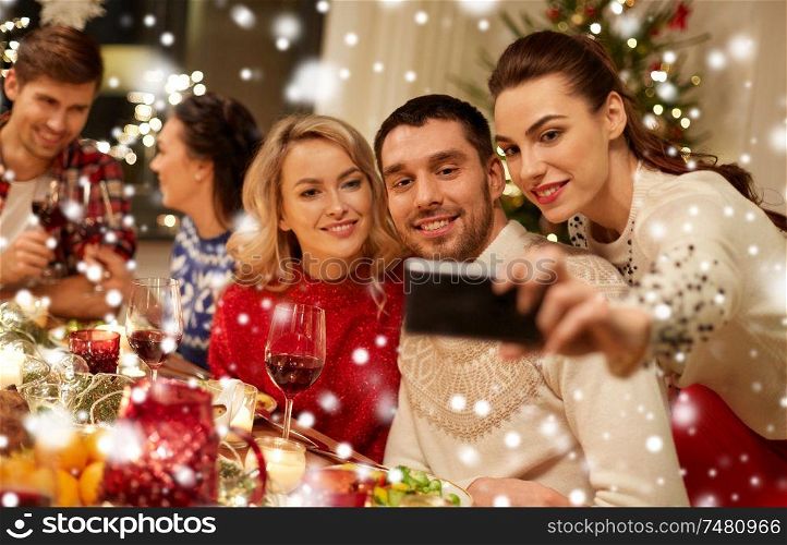 holidays and celebration concept - happy friends having christmas dinner at home and taking selfie by smartphone over snow. friends having christmas dinner and taking selfie