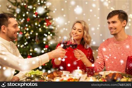 holidays and celebration concept - happy friends having christmas dinner at home, drinking red wine and clinking glasses over snow. happy friends drinking red wine at christmas party
