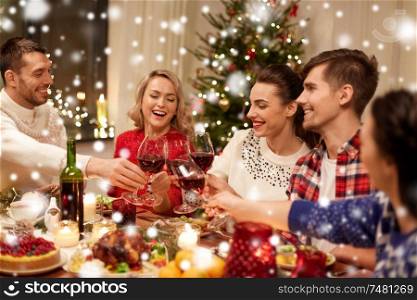 holidays and celebration concept - happy friends having christmas dinner at home, drinking red wine and clinking glasses over snow. friends celebrating christmas and drinking wine