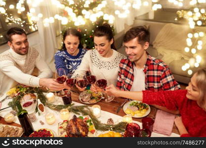 holidays and celebration concept - happy friends having christmas dinner at home, drinking red wine and clinking glasses. friends celebrating christmas and drinking wine