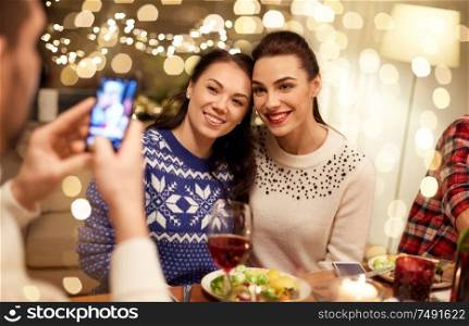 holidays and celebration concept - happy friends having christmas dinner at home and taking picture by smartphone. friends having christmas dinner and taking picture
