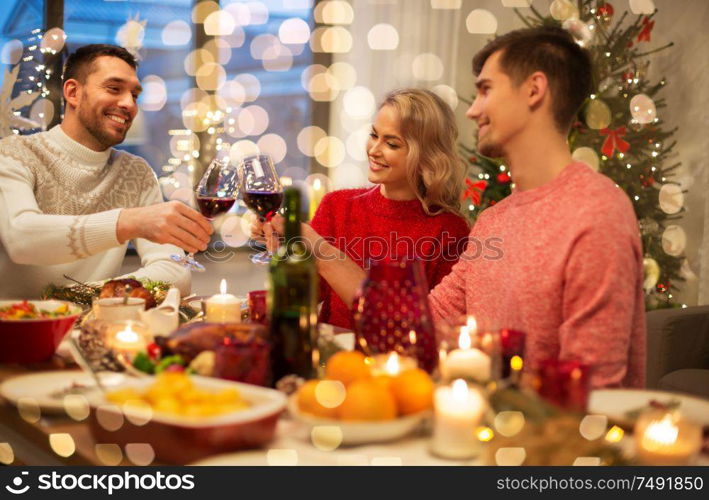 holidays and celebration concept - happy friends having christmas dinner at home, drinking red wine and clinking glasses. happy friends drinking red wine at christmas party