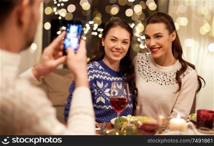holidays and celebration concept - happy friends having christmas dinner at home and taking picture by smartphone. friends having christmas dinner and taking picture