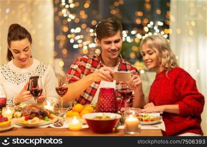 holidays and celebration concept - happy friends having christmas dinner at home and photographing food by smartphone. happy friends having christmas dinner at home