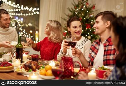 holidays and celebration concept - happy friends having christmas dinner at home, drinking red wine and clinking glasses. happy friends having christmas dinner at home