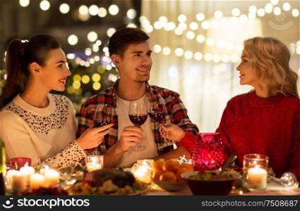 holidays and celebration concept - happy friends having christmas dinner at home, drinking red wine and clinking glasses. happy friends drinking red wine at christmas party