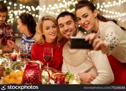 holidays and celebration concept - happy friends having christmas dinner at home and taking selfie by smartphone. friends having christmas dinner and taking selfie