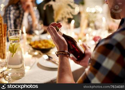 holidays and celebration concept - happy friends having christmas dinner at home with bottle of non-alcoholic red wine. happy friends with red wine at christmas party