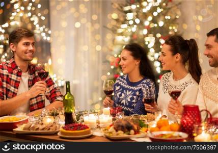 holidays and celebration concept - happy friends having christmas dinner at home and drinking red wine. happy friends drinking red wine at christmas party