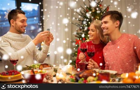 holidays and celebration concept - happy friends photographing at christmas dinner over snow. happy friends photographing at christmas dinner