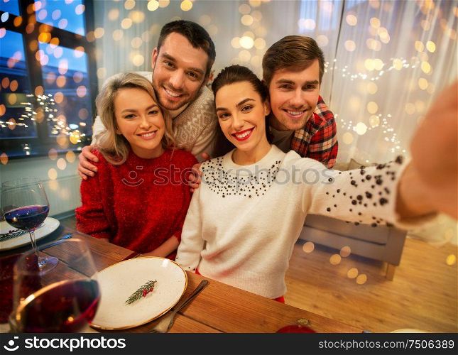 holidays and celebration concept - happy friends taking selfie at home christmas dinner. friends taking selfie at christmas dinner