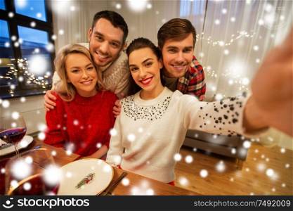 holidays and celebration concept - happy friends taking selfie at home christmas dinner over snow. friends taking selfie at christmas dinner