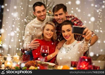 holidays and celebration concept - happy friends taking selfie by smartphone at home christmas dinner over snow. friends taking selfie at christmas dinner