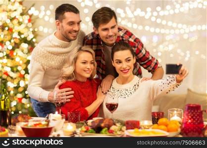 holidays and celebration concept - happy friends taking selfie by smartphone at home christmas dinner. friends taking selfie at christmas dinner