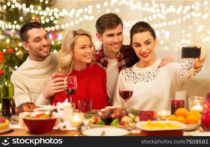 holidays and celebration concept - happy friends taking selfie by smartphone at home christmas dinner. friends taking selfie at christmas dinner
