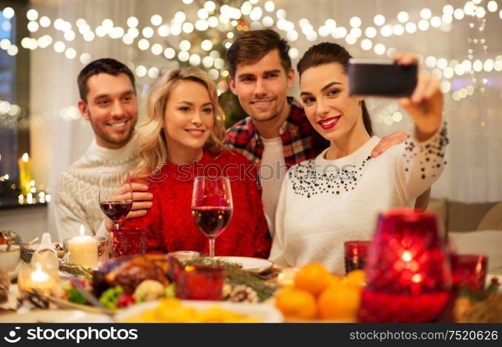 holidays and celebration concept - happy friends taking selfie by smartphone at home christmas dinner. friends taking selfie at christmas dinner