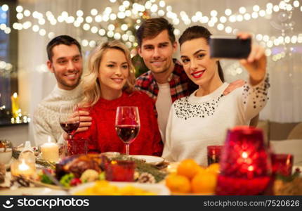 holidays and celebration concept - happy friends taking selfie by smartphone at home christmas dinner. friends taking selfie at christmas dinner