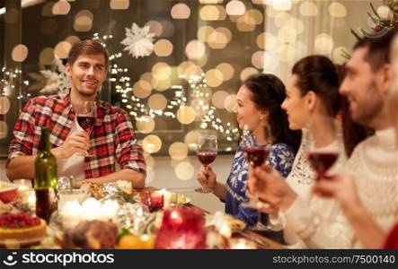 holidays and celebration concept - happy friends with glasses of wine having christmas dinner and speaking toast at home. friends celebrating christmas and speaking toast