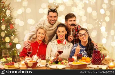 holidays and celebration concept - happy friends with party props having christmas dinner at home. happy friends celebrating christmas at home