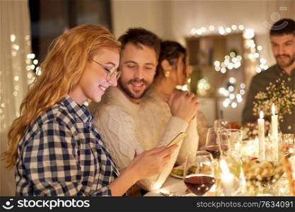 holidays and celebration concept - happy friends with smartphone having christmas dinner party at home. friends with cellphone having dinner party at home