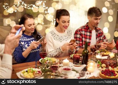 holidays and celebration concept - happy friends with smartphones having christmas dinner at home. friends with smartphones having christmas dinner