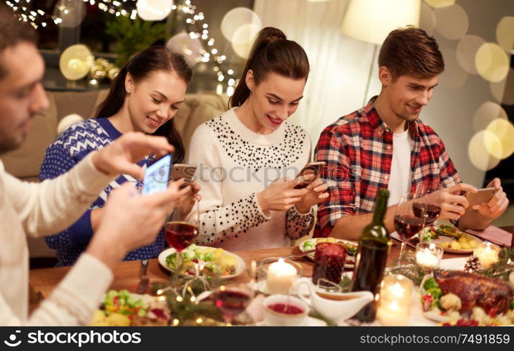 holidays and celebration concept - happy friends with smartphones having christmas dinner at home. friends with smartphones having christmas dinner