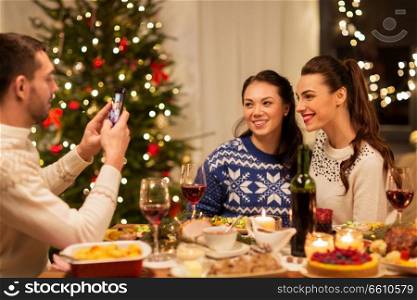 holidays and celebration concept - happy man photographing his friends at christmas dinner. happy friends photographing at christmas dinner