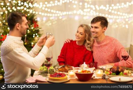 holidays and celebration concept - happy man photographing his friends at christmas dinner. happy friends photographing at christmas dinner