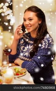 holidays and celebration concept - happy woman calling on smartphone while having christmas dinner at home over snow. woman calling on smartphone at christmas dinner