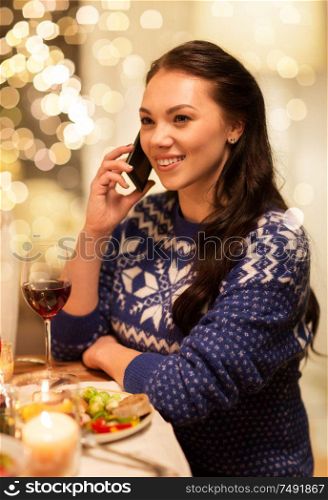 holidays and celebration concept - happy woman calling on smartphone while having christmas dinner at home. woman calling on smartphone at christmas dinner