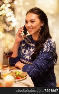 holidays and celebration concept - happy woman calling on smartphone while having christmas dinner at home. woman calling on smartphone at christmas dinner