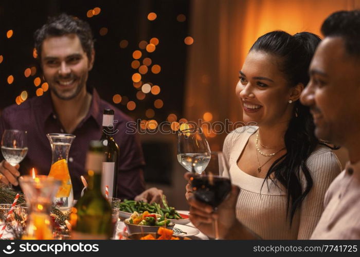 holidays and celebration concept - happy woman having christmas dinner with friends and drinking wine at home. happy friends drinking wine at christmas dinner