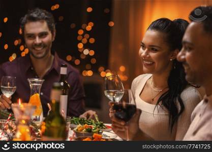 holidays and celebration concept - happy woman having christmas dinner with friends and drinking wine at home. happy friends drinking wine at christmas dinner