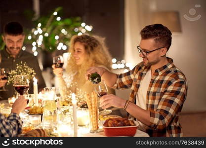 holidays and celebration concept - happy young man pouring non-alcoholic red wine to glass at christmas dinner party at home. man pouring red wine to glass at dinner party