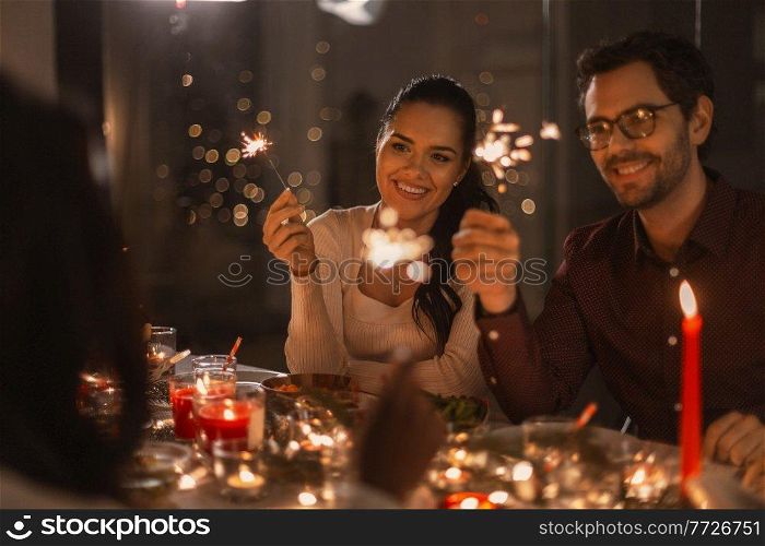 holidays and celebration concept - multiethnic group of happy friends with sparklers having christmas dinner at home. happy friends with sparklers at christmas dinner