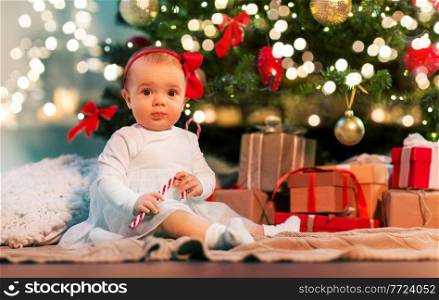 holidays and childhood concept - cute baby girl at christmas tree with gifts at home. baby girl under christmas tree with gifts at home