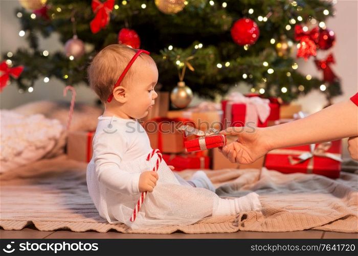 holidays and childhood concept - sweet baby girl at christmas tree with gifts at home. baby girl at christmas tree with gifts at home