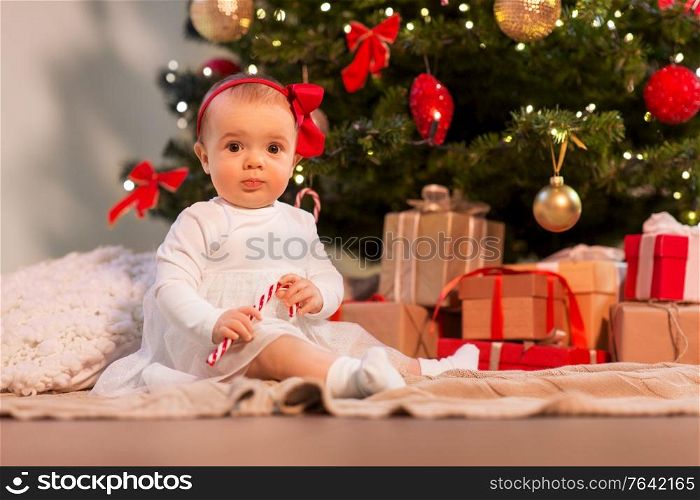 holidays and childhood concept - sweet baby girl at christmas tree with gifts at home. baby girl at christmas tree with gifts at home